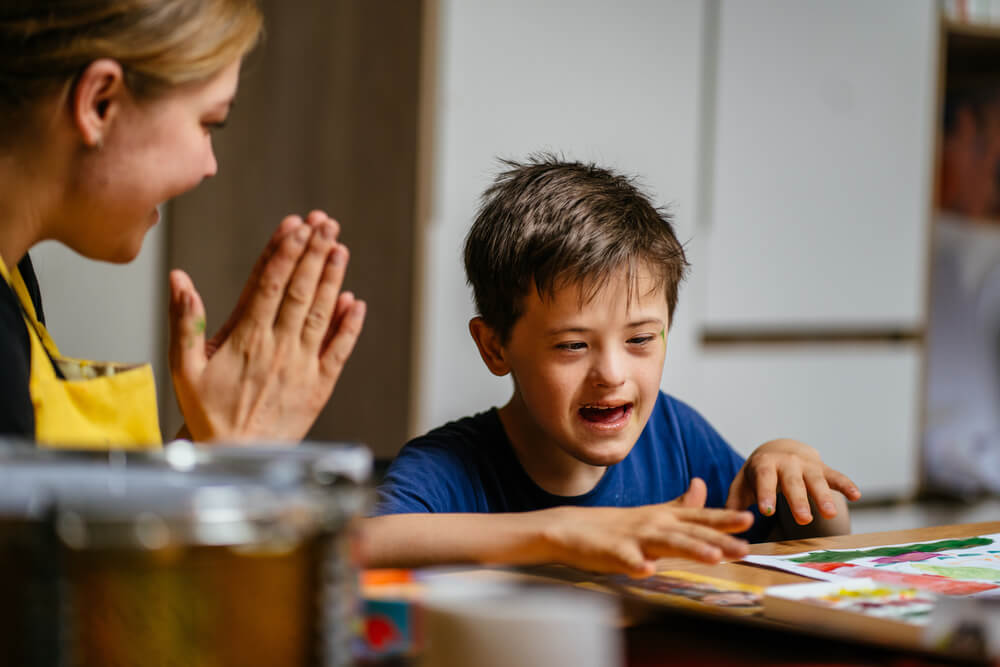 The teacher claps her hands and rejoices at the small victory of her student boy with down syndrome.