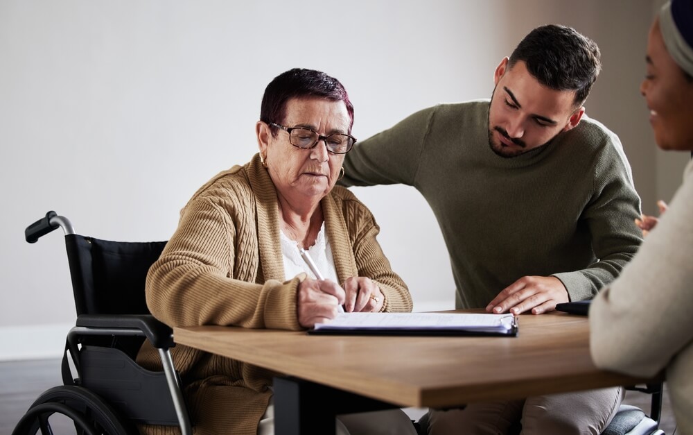 Disabled senior with her guardian signing document.