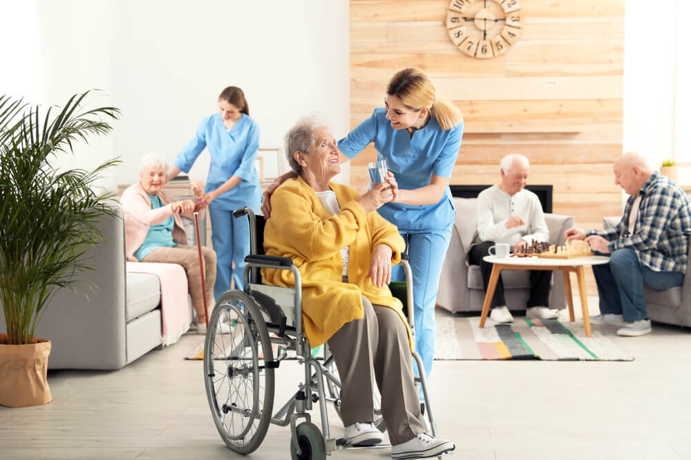 Nurse giving glass of water to elderly woman in wheelchair at nursing home.